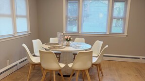 Un coin repas avec une table ronde, six chaises et un vase de fleurs.