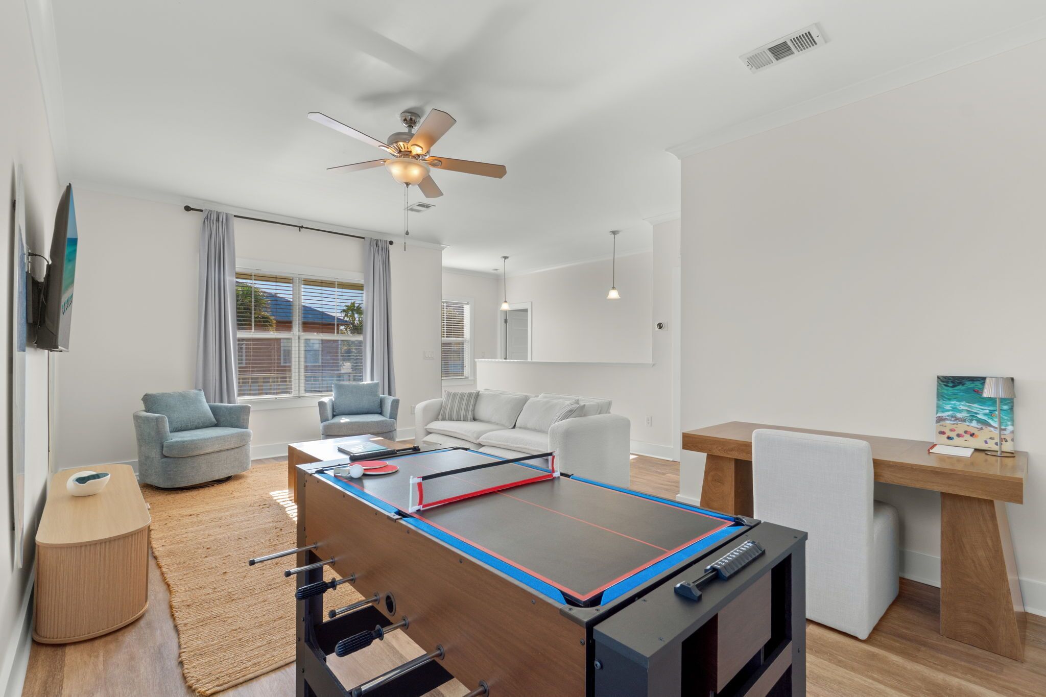 Een moderne woonkamer met een tafelvoetbaltafel, een plafondventilator en een groot raam met gordijnen.