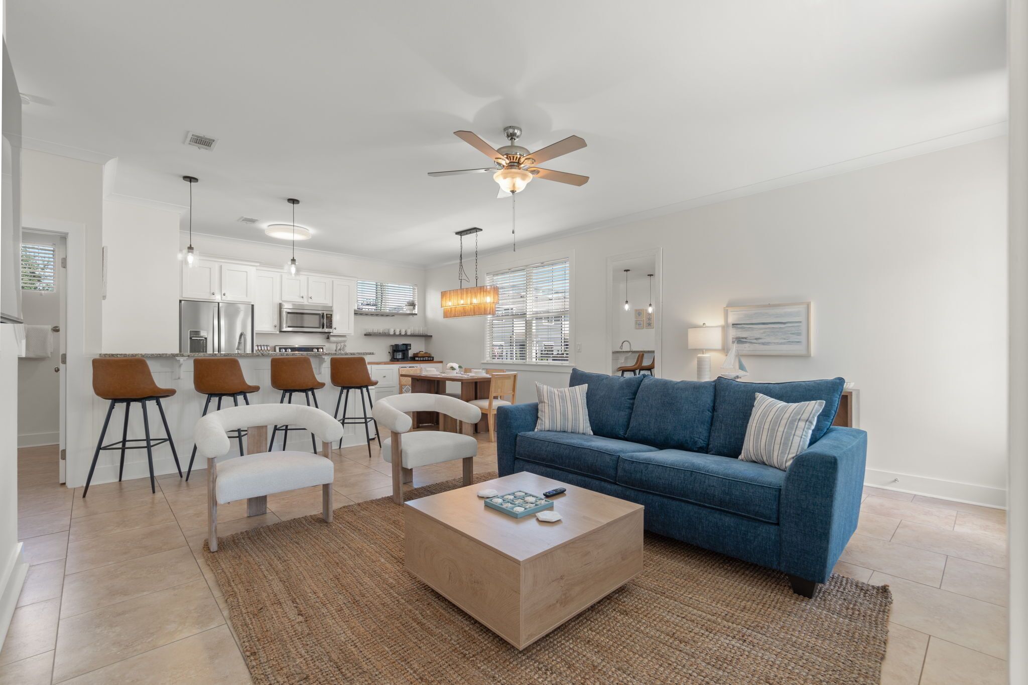 A modern living room with a blue sofa, white chairs, a coffee table, and a ceiling fan.