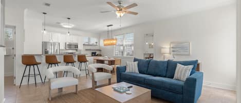 A modern living room with a blue sofa, white chairs, a coffee table, and a ceiling fan.