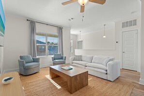 Ein modernes Wohnzimmer mit einer Couch, zwei Sesseln, einem Couchtisch aus Holz und einem Deckenventilator.