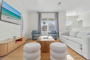 A modern living room with a sofa, two armchairs, a coffee table, and a TV displaying a beach scene. - Sleeps 10 l 3 Min to Beach l Pool l Game Room l Wireless Internet l Pompano Joes (Miramar Beach)