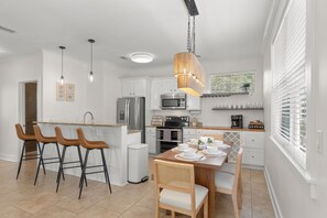 Une cuisine moderne avec des meubles blancs, des appareils en acier inoxydable et un coin repas comprenant une table et des chaises en bois.