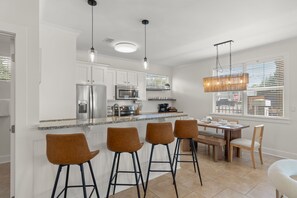 A modern kitchen with white cabinets, stainless steel appliances, a granite countertop, and a bar area with stools. - Sleeps 10 l 3 Min to Beach l Pool l Game Room l Wireless Internet l Pompano Joes (Miramar Beach)