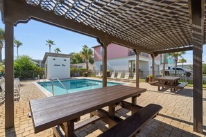 Ein überdachter Poolbereich mit einem Holztisch und Liegestühlen.
