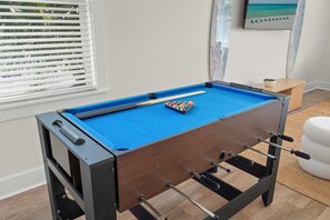 A foosball table in a room with a window, a small table, and a wall-mounted artwork. - Sleeps 10 l 3 Min to Beach l Pool l Game Room l Wireless Internet l Pompano Joes (Miramar Beach)