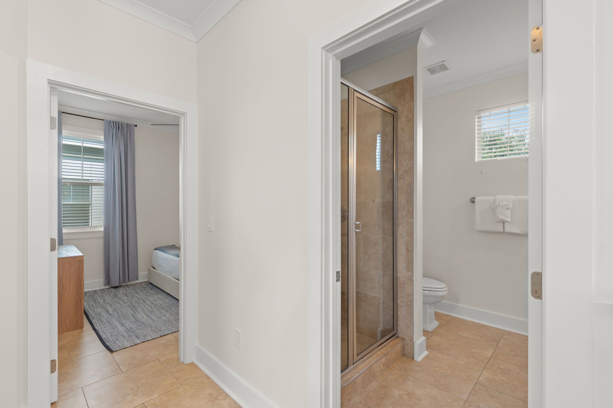 Ein modernes Badezimmer mit Duschabtrennung aus Glas, Toilette und einem Fenster mit Jalousien.