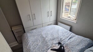 Un dormitorio con cama, radiador, ventana y armario.
