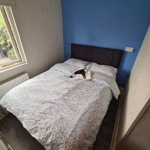 A single bed with a patterned bedspread, a headboard, and a window with a view of greenery. - Private Apartment (Flat 3) (Dublin)