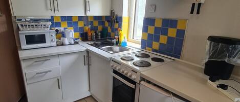 Une cuisine de taille réduite avec des meubles blancs, un four à micro-ondes, une cuisinière et un lave-vaisselle.