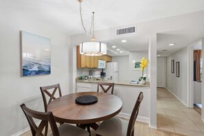 A modern kitchen with wooden cabinets, a built-in oven, and a dining area with a round table and chairs. - D-226 - Peaceful Views on Quiet End of Resort (Naples)