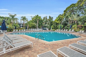 A rectangular swimming pool surrounded by lounge chairs and umbrellas, with a tiled deck and tropical vegetation. - D-226 - Peaceful Views on Quiet End of Resort (Naples)