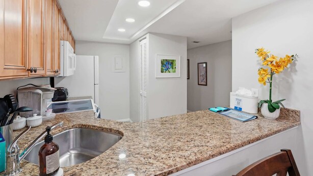 Una cocina con encimeras de granito, pileta de acero inoxidable, muebles de madera y un refrigerador blanco.