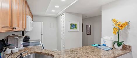 Una cocina con encimeras de granito, pileta de acero inoxidable, muebles de madera y un refrigerador blanco.