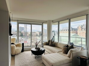 A modern living room with a large window, a sofa, a chair, and a coffee table. - The Falls - Downtown Victoria, where luxury living meets panoramic views. (Victoria)