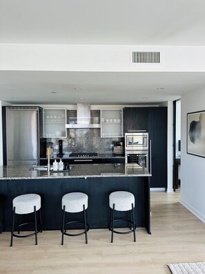 A modern kitchen with a central island, bar stools, and a microwave. - The Falls - Downtown Victoria, where luxury living meets panoramic views. (Victoria)