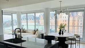 Eine moderne Küche mit einer großen Kücheninsel, einem Essbereich mit Stühlen und großen Fenstern, die einen Blick auf die Stadt ermöglichen.