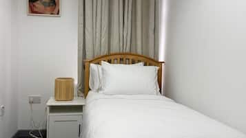A single-bed room with a wooden headboard, a bedside table with a lamp, and a wall-mounted picture frame.