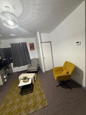 A compact living space with a kitchenette, a dining area, and a seating area with a yellow armchair and a small table with a plant. - Modern apartment close to city centre (Manchester)