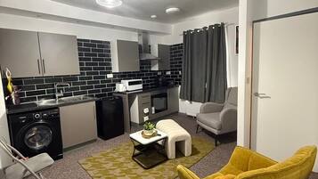 A compact living space with a kitchenette, a sofa, a yellow armchair, and a small table with a plant.