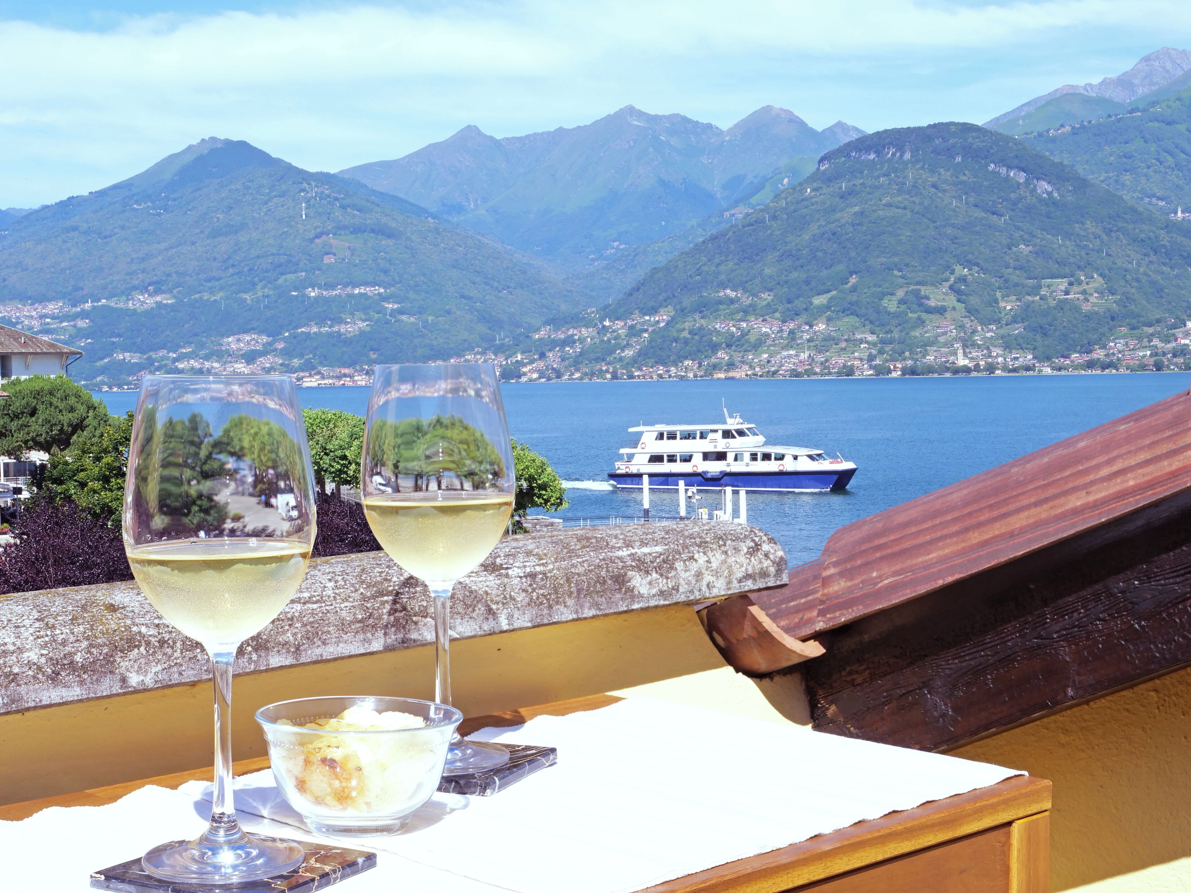 Two glasses of white wine on a table with a view of a lake and mountains.