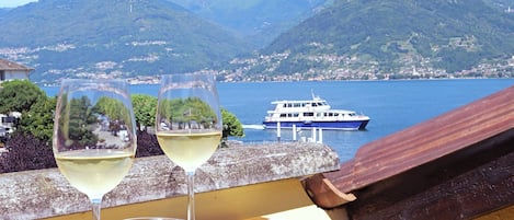 Two glasses of white wine on a table with a view of a lake and mountains.
