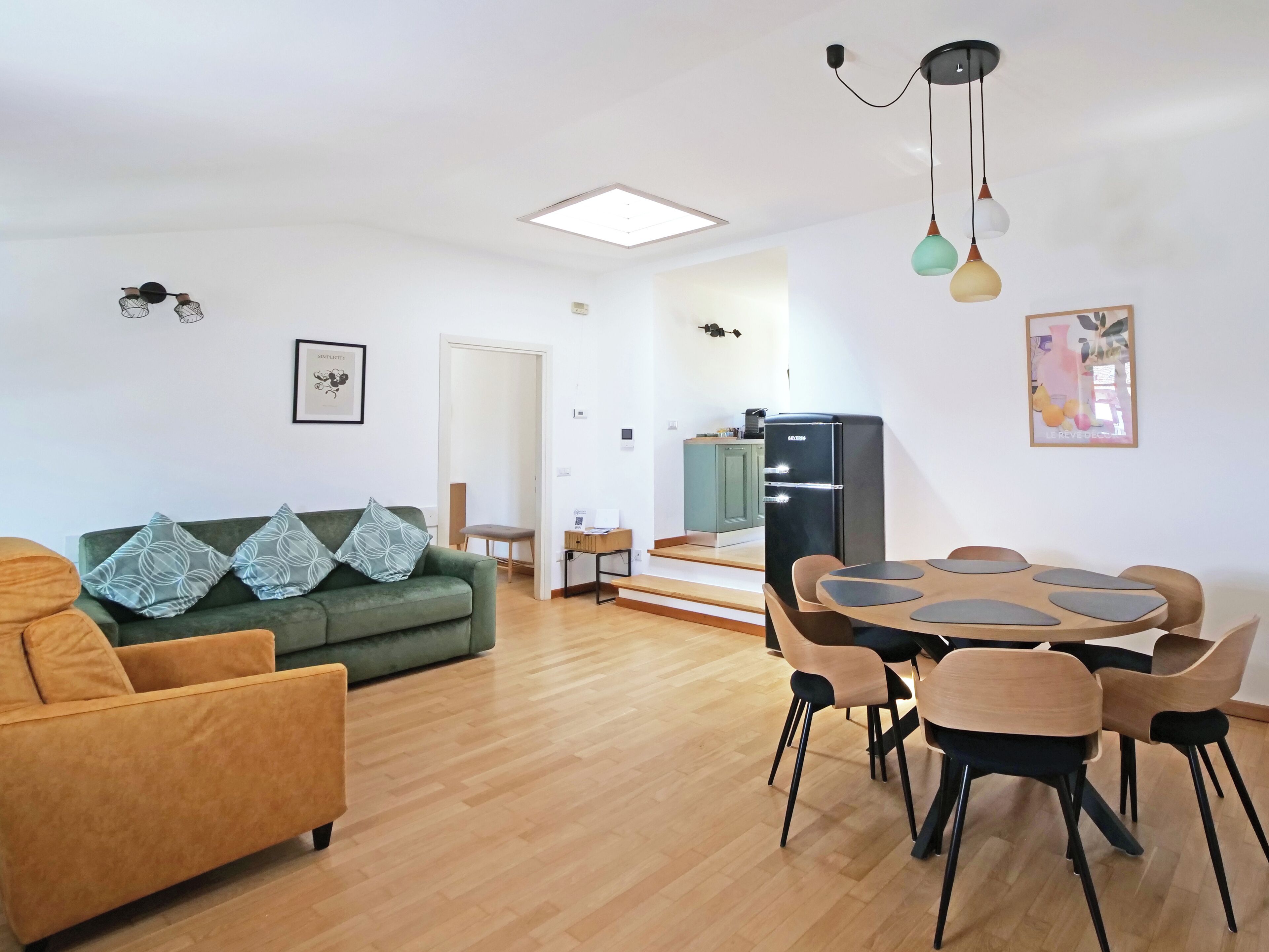 Een moderne woonkamer met een bank, eettafel en stoelen. Achtergrond toont een keuken.