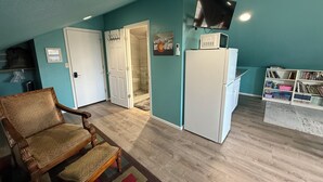 A room with a wooden floor, a white refrigerator, a television mounted on the wall, and a bookshelf filled with books.