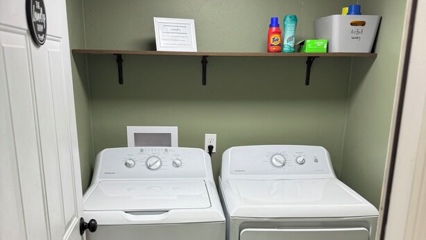 A laundry room with two front-loading washing machines, a shelf with laundry supplies, and a door with a lock.