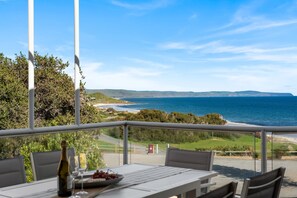 A dining area with a table and chairs, overlooking a coastal landscape with hills and the sea. - Carrickalinga House A Symphony of Sea and Serenity (Carrickalinga)