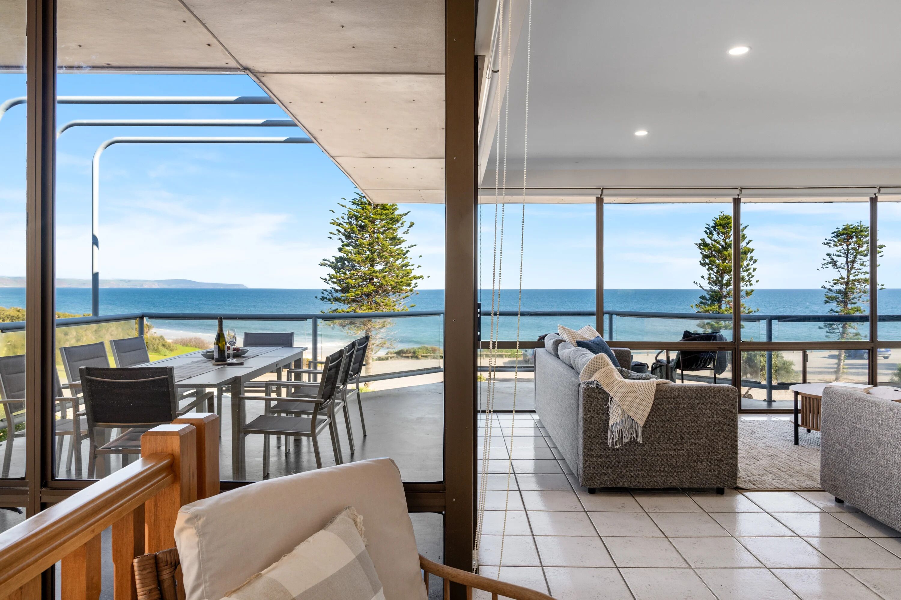 A modern interior with a large balcony overlooking the sea, furnished with a sofa, chairs, and a dining table.