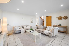 A modern living room with two sofas, a coffee table, and a wooden staircase. - Carrickalinga House A Symphony of Sea and Serenity (Carrickalinga)