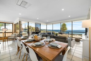 A spacious dining area with a view of the sea, a cozy seating area with a sofa, and a table set for a meal. - Carrickalinga House A Symphony of Sea and Serenity (Carrickalinga)