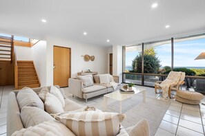 A modern living room with a sofa, coffee table, and a view of the outdoors. - Carrickalinga House A Symphony of Sea and Serenity (Carrickalinga)