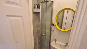 Un bagno con doccia, lavandino, servizi igienici e uno specchio dalla cornice gialla.