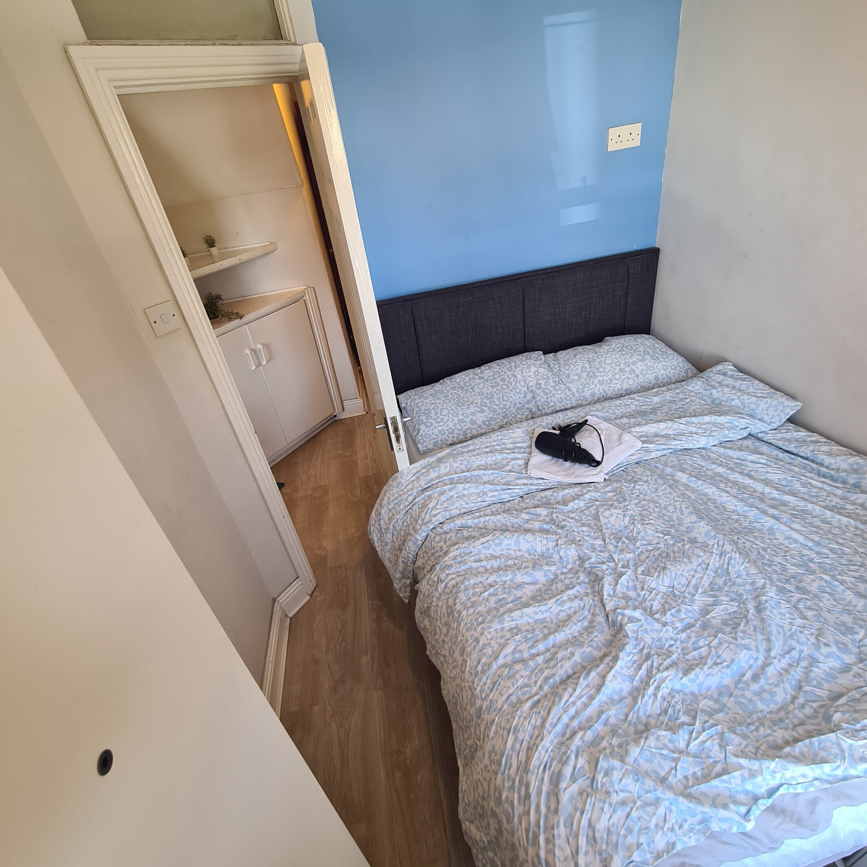 A bedroom with a bed, a nightstand, a wardrobe, and a blue wall.