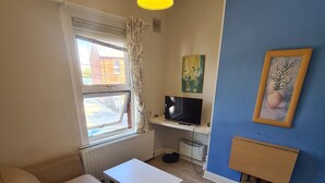 Un ambiente compatto con un divano, un tavolino, una TV e un termosifone.