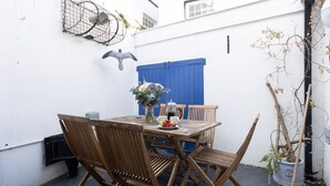 A wooden table with chairs, a vase of flowers, and a coffee pot on a balcony. - Quayside retreat with stunning estuary views (Appledore)