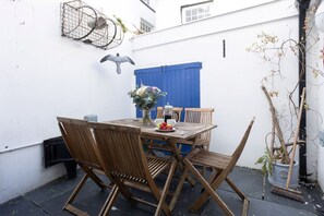 A wooden table with chairs, a vase of flowers, and a coffee pot on a balcony. - Quayside retreat with stunning estuary views (Appledore)
