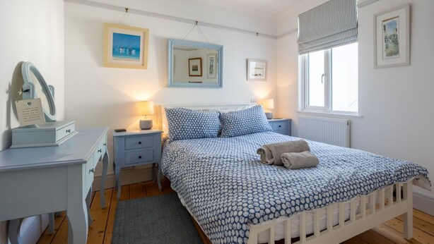 A bedroom with a bed, bedside tables, a dresser, a mirror, and framed pictures on the walls. - Quayside retreat with stunning estuary views (Appledore)