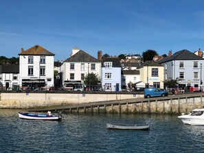 Une promenade en bord de mer bordée d’immeubles, avec un bateau amarré et un chemin piétonnier.
