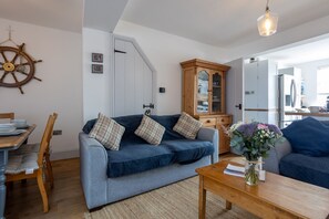 Un salon comprenant un canapé, un meuble en bois, une table à manger avec des chaises et une décoration murale représentant un gouvernail de bateau.