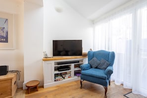 A living room with a television on a white entertainment unit, a blue armchair, and a small wooden table. - Quayside retreat with stunning estuary views (Appledore)