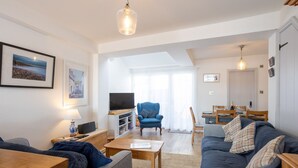 A spacious living area with a sofa, a television, a dining table, and a blue armchair. - Quayside retreat with stunning estuary views (Appledore)