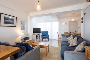 A spacious living area with a sofa, a television, a dining table, and a blue armchair. - Quayside retreat with stunning estuary views (Appledore)