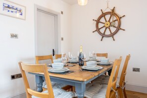 A dining area with a wooden table set for six, surrounded by chairs with cushioned seats. - Quayside retreat with stunning estuary views (Appledore)