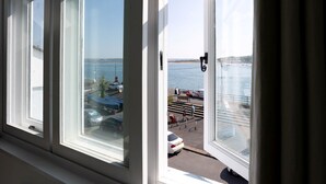 A view from a window overlooking a waterfront area with parked cars and a pedestrian walkway. - Quayside retreat with stunning estuary views (Appledore)