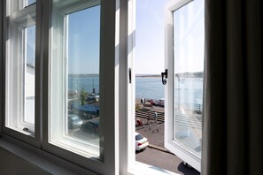 A view from a window overlooking a waterfront area with parked cars and a pedestrian walkway. - Quayside retreat with stunning estuary views (Appledore)