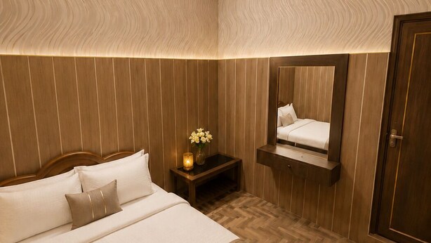 A modern bedroom with a large bed, a bedside table with a vase of flowers, and a mirror above the bed. - Hotel New Lucknow (Lucknow)