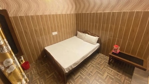 A bedroom with a bed, a bedside table, a red bucket, and a patterned floor. - Hotel New Lucknow (Lucknow)